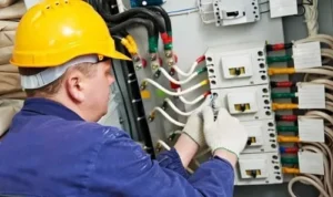 a commercial electrician in a yellow hard hat repairing an industrial electrical panel with colorful wiring, emphasizing commercial electrical services in Los Angeles County.